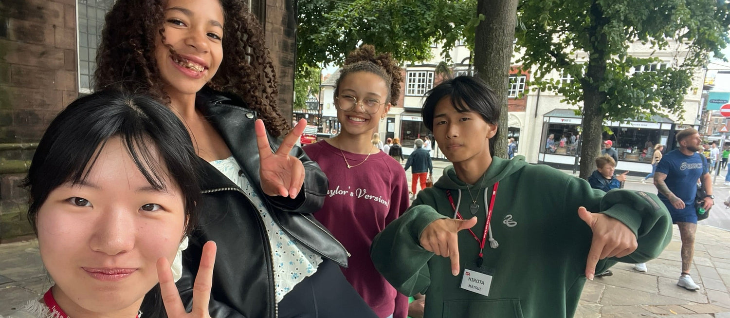 Four young people posing for a photo outdoors with trees and buildings in the background.