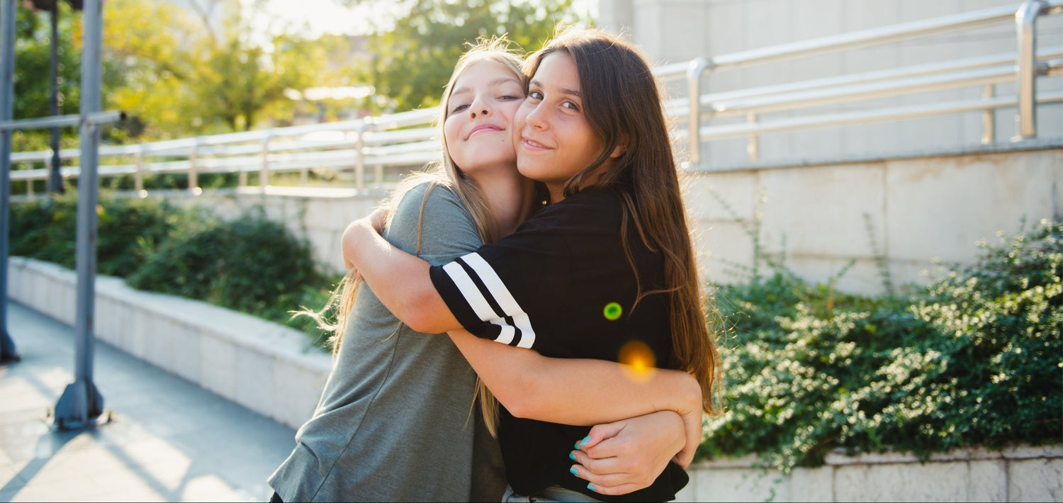 Two people hugging outdoors with a building and greenery in the background